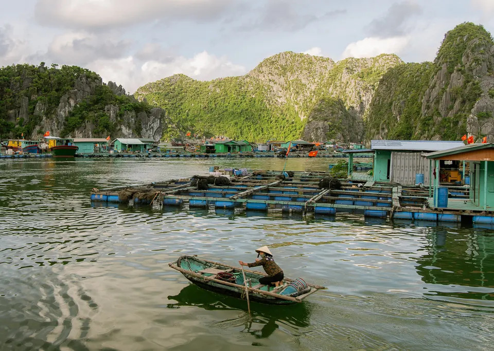 A woman rowing a small boat past floating houses in a fishing village