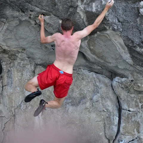 A climber in red shorts pulling up a limestone face