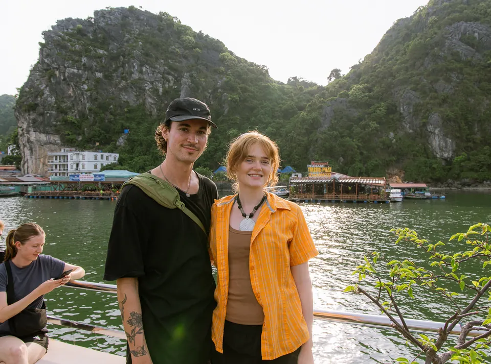 Two travellers on a boat deck with the cliffs of Lan Ha Bay behind them