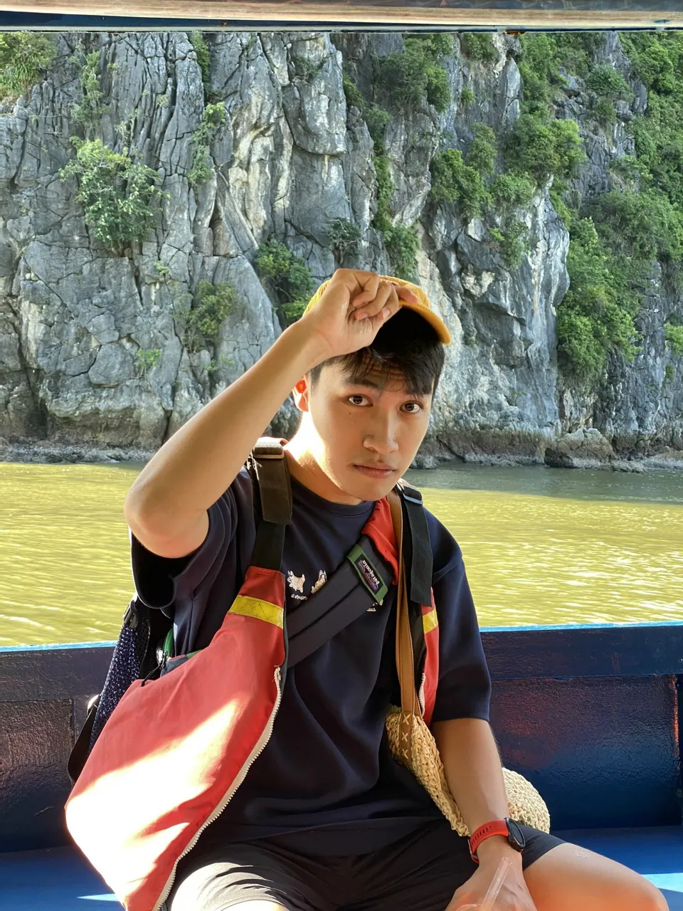 A guest with a backpack smiling on a boat deck in front of a limestone cliff