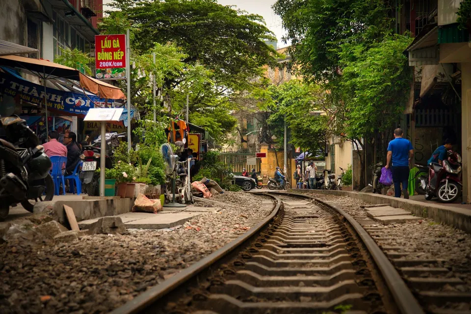 Railway tracks running through the cafes of Train Street in Hanoi, with plastic stools, stalls and parked motorbikes alongside