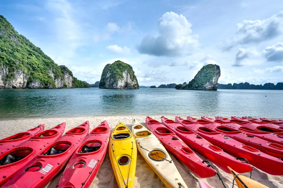 Red and yellow kayaks lined up on a small beach facing the karsts of Lan Ha Bay