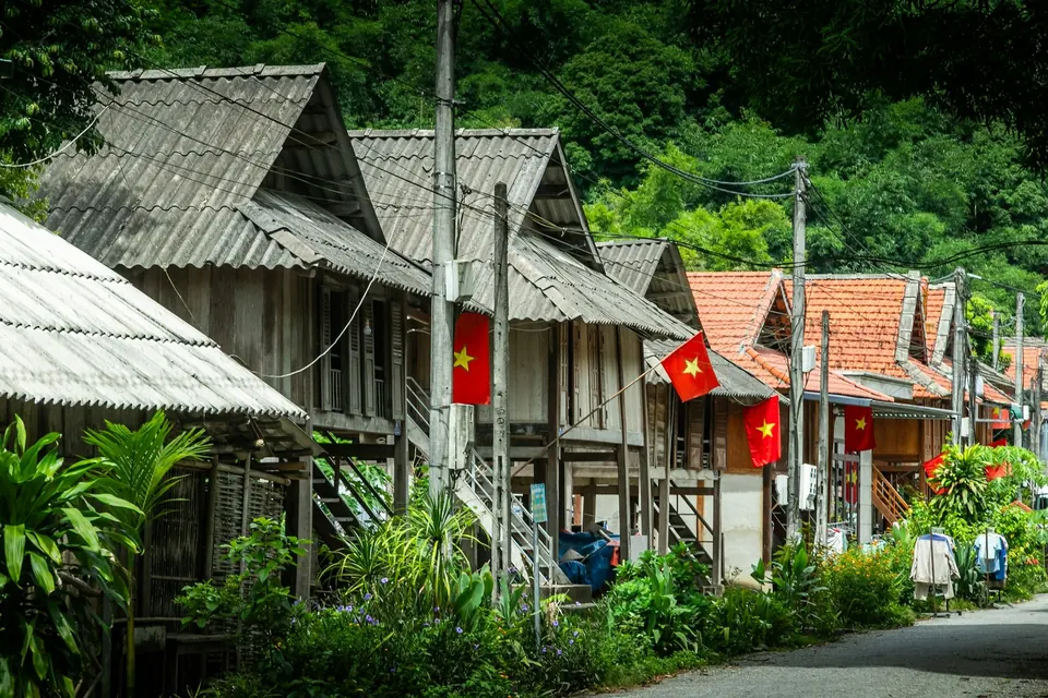 White Thai stilt houses with tiled roofs along a village road in Mai Chau, Vietnam, forested mountain behind