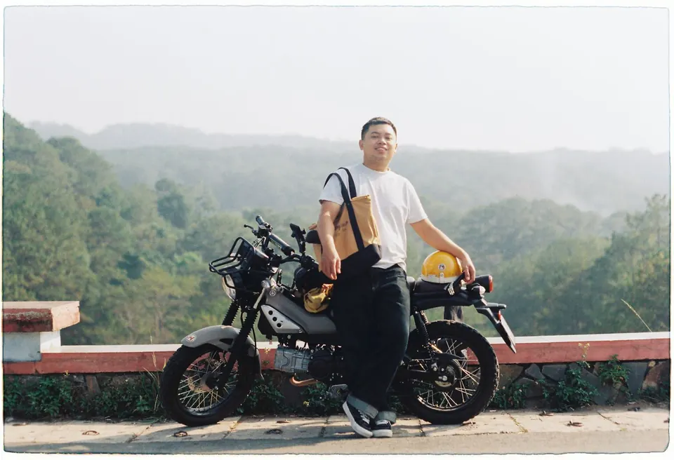 A rider beside a motorbike at a viewpoint above misty hills