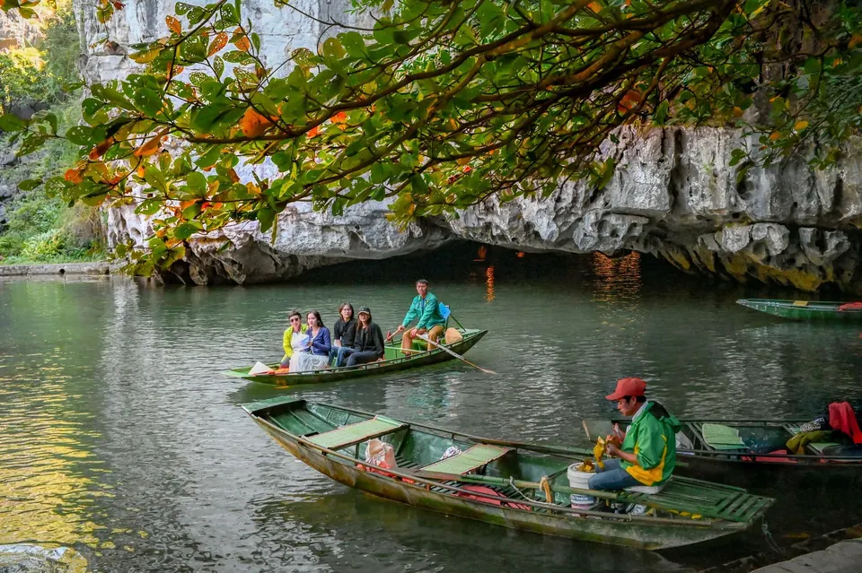 Wooden sampans and a rower at the mouth of a limestone cave in Trang An, Ninh Binh