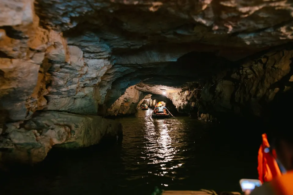 A rowboat inside a lit limestone water cave in Trang An, Ninh Binh, passengers in orange life jackets