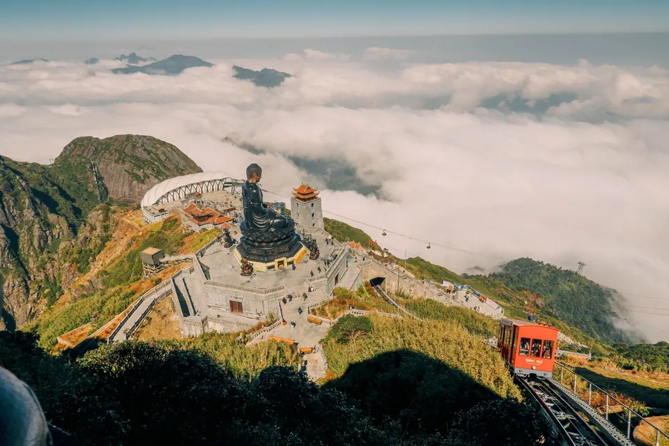 The Fansipan summit complex above a sea of clouds in Lao Cai, with the bronze Buddha statue and the mountain train on the slope