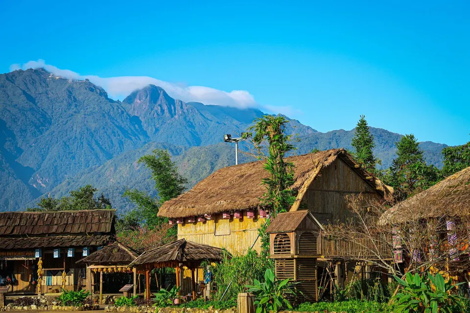Traditional wooden houses with thatched roofs in a village near Sapa, the Fansipan ridge with cloud behind
