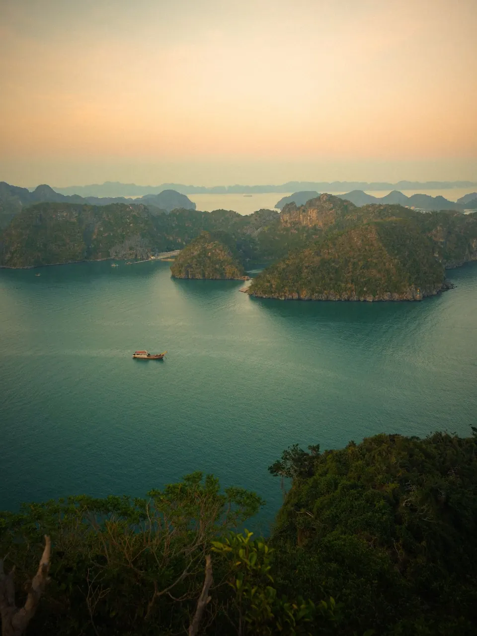 Lan Ha Bay at golden hour seen from a hilltop above Cat Ba, one small boat crossing the water