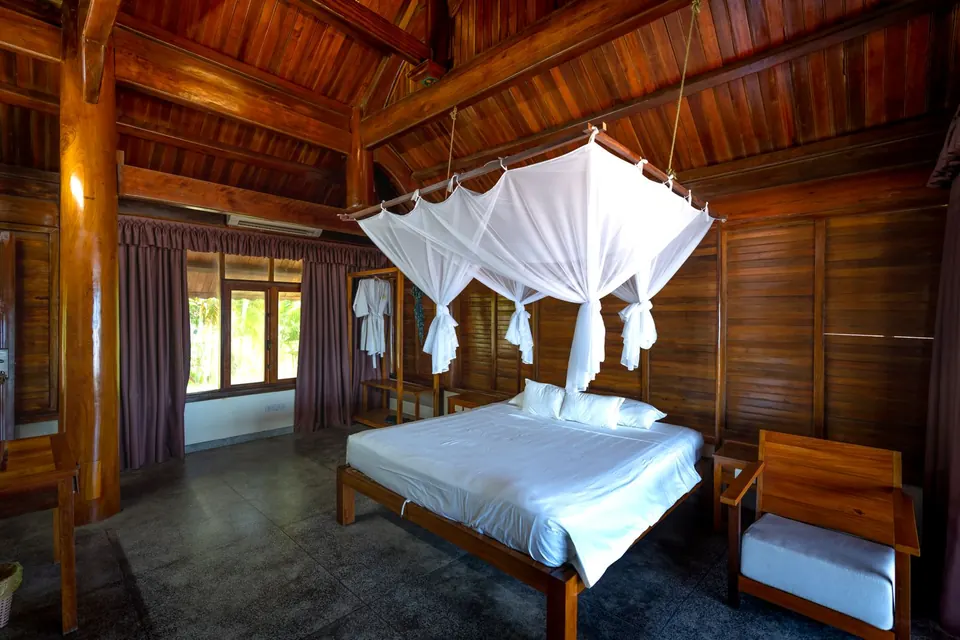 A wooden bungalow room with a mosquito net over the bed